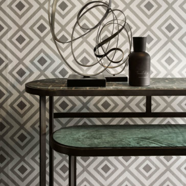 Modern Console Table Set The interior display is anchored by the Modern Console Table Set, complemented by geometric wallpaper with diamond patterns. The metal-framed table showcases a contemporary abstract metal sculpture and an opaque dark bottle, resulting in an aesthetically pleasing and minimalist arrangement.