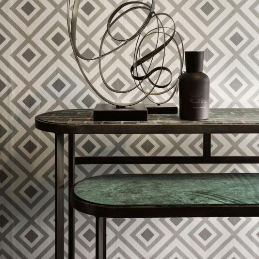 Modern Console Table Set The interior display is anchored by the Modern Console Table Set, complemented by geometric wallpaper with diamond patterns. The metal-framed table showcases a contemporary abstract metal sculpture and an opaque dark bottle, resulting in an aesthetically pleasing and minimalist arrangement.