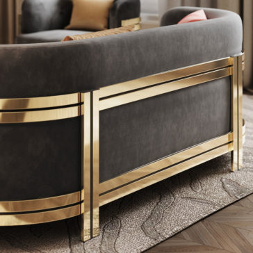 A close-up of the **Modern Curved Sofa With Brass Frame** showcases its luxurious design with a dark backrest elegantly enclosed by the brass frame. The sofa is situated on a textured carpet, with part of a cushioned chair visible in the background.