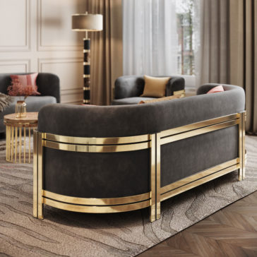 A luxurious living room features the Modern Curved Sofa With Brass Frame in sleek black, enhanced with gold accents. It is complemented by a matching armchair and a round glass coffee table with a gold base. The room boasts light-colored walls, a tall floor lamp, a large window adorned with sheer curtains, and a textured rug.