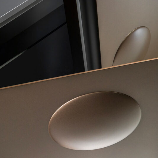 Modern Industrial 4 Door Sideboard A detailed view of the Modern Industrial 4 Door Sideboard showcases its sleek structure, with overlapping panels and a circular indentation on one. The panels have a smooth, brushed bronze finish with a subtle gradient, set against a predominantly dark background accented by metallic reflections.