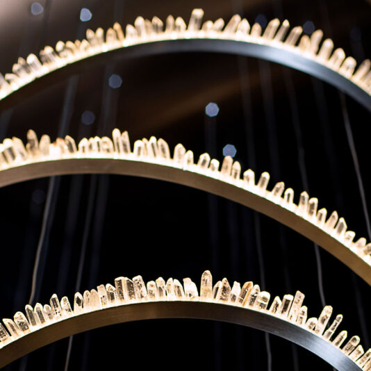 Modern Quartz Crystal Hoop Chandelier Close-up of three circular metal rings adorned with vertical quartz crystal-like structures, illuminated against a dark background. The crystals catch the light, creating a sparkling effect that adds a sense of modern elegance and intrigue, reminiscent of the Modern Quartz Crystal Hoop Chandelier.