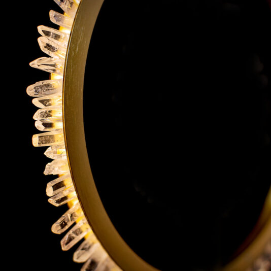 Modern Quartz Crystal Hoop Chandelier A close-up of the Modern Quartz Crystal Hoop Chandelier against a dark background. The circular fixture exhibits an intricate, radiant design with clear, angular crystals projecting from its edge, backlit to create a striking contrast against the darkness.