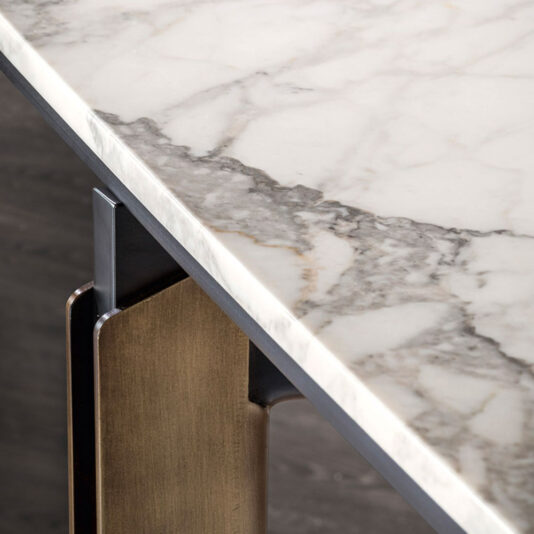 Modern Rectangular Marble Dining Table A close-up view of the corner of the Modern Rectangular Marble Dining Table reveals its marble top featuring a white and gray veined pattern. The legs, crafted from a combination of brushed bronze and dark metal, highlight an elegant contrast between materials and textures.