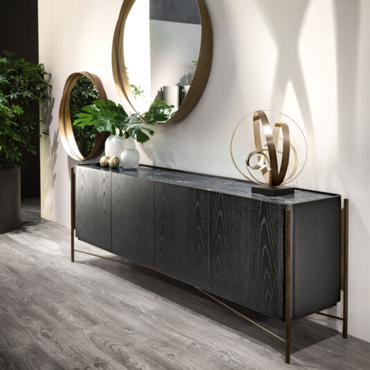 Modern Twisted Bronze Table Lamp A modern hallway with a dark wood console table featuring a marble top. Atop the console are decorative gold spheres, an abstract gold sculpture, and the Modern Twisted Bronze Table Lamp. A large round mirror with a gold frame hangs above the console, with green potted plants nearby.