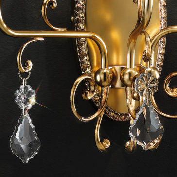 Close-up of the Traditional Crystal Pendant Wall Light, an ornate, gold-colored wall sconce with intricate detailing. This elegant fixture features two large, dangling clear crystal ornaments that refract light beautifully, creating a sparkling effect akin to a crystal pendant. The solid dark backdrop accentuates the brilliance of the wall light.