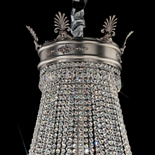 Antiqued Chrome Crystal Empire Chandelier A detailed view of the Antiqued Chrome Crystal Empire Chandelier reveals ornate metalwork at its top, embellished with delicate leaf designs. Numerous glittering crystal strands cascade downward, enhancing its luxurious and elegant look against a black background.
