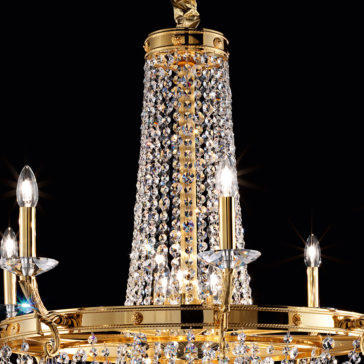 Classic Crystal Drop Chandelier The Classic Crystal Drop Chandelier is a luxurious fixture adorned with sparkling crystals and gold accents. It features five candle-like light bulbs extending outward, illuminating the crystal strands cascading from the top. The intricate details are particularly striking against a dark background.