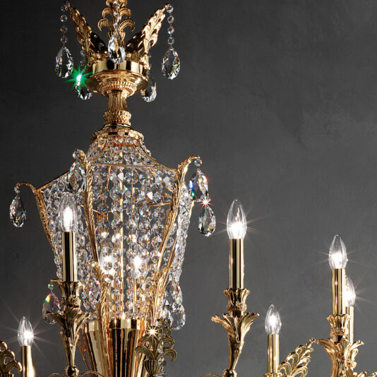 A close-up of the Classic Gold Plated Crystal Empire Chandelier, adorned with numerous crystals. The chandelier features multiple candle-like light bulbs emitting a soft, warm light that enhances the sparkle of the crystals. The background is a dark gray wall.