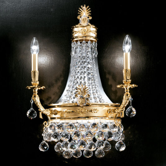 An ornate Classic Crystal Empire Style Wall Light is mounted on a black wall. This two-light sconce features intricate detailing with crystal embellishments, a central draped crystal design, and candle-style light bulbs on either side, each topped with small flame-shaped bulbs.