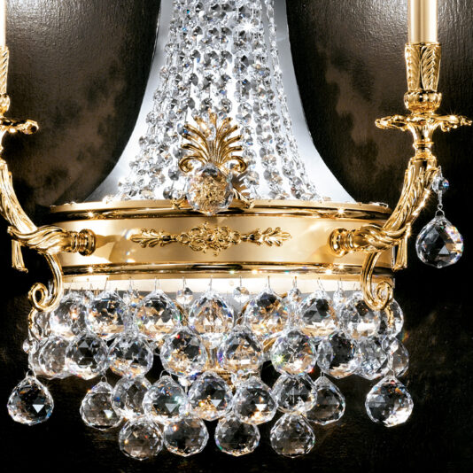 Classic Crystal Empire Style Wall Light The Classic Crystal Empire Style Wall Light is an ornate, gold-plated sconce featuring two candle-style lights. The centerpiece boasts an intricate design adorned with clear, hanging crystal ornaments that catch the light and sparkle beautifully. This elegant wall light stands out exquisitely against a dark, sophisticated backdrop.