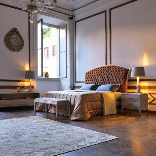 Luxurious bedroom featuring the Classic Italian Button Upholstered Bed with a high tufted headboard, a large window showcasing an exterior view, an elegant pendant chandelier, and stylish wooden furniture. The room also includes soft lighting from bedside lamps and a patterned rug laid on wood-paneled flooring.