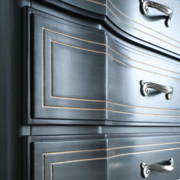 Classic Style Italian Chest Of Drawers Close-up view of the Classic Style Italian Chest Of Drawers, showcasing its elegant dark wooden finish with ornate silver handles and decorative gold trim on the drawers. The glossy surface highlights the intricate detailing, reminiscent of a timeless piece.