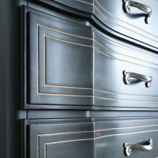 Close-up view of the Classic Style Italian Chest Of Drawers, showcasing its elegant dark wooden finish with ornate silver handles and decorative gold trim on the drawers. The glossy surface highlights the intricate detailing, reminiscent of a timeless piece.