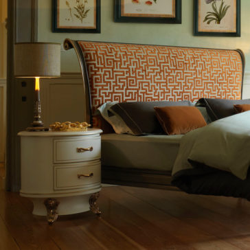 Classic Style Upholstered Sleigh Bed A cozy bedroom showcases the Classic Style Upholstered Sleigh Bed, highlighted by its ornate orange and white patterned headboard. The bed is adorned with brown and green pillows for added comfort. Beside the bed sits a white nightstand with gold hardware, topped with a lamp. Wooden flooring and framed botanical prints further enhance the room's warm ambiance.