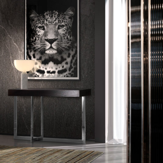 A modern interior featuring a Modern Black Console Table With Drawer and a white lamp. Behind the table, a large black-and-white leopard photograph dominates the wall. Light filters in through a sheer curtain on the right, illuminating the space with a soft glow.