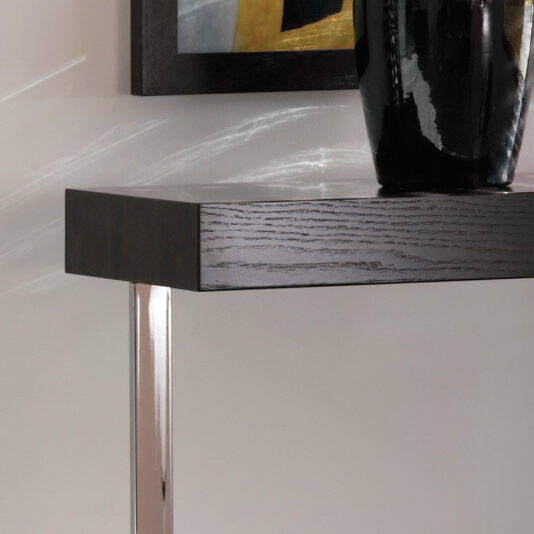 A close-up of the Modern Black Console Table With Drawer showcases its dark wooden top and metallic legs. Adorning the sleek table is a shiny black vase. Positioned against a light-colored wall, the setting also includes a framed abstract painting partially visible in the background.