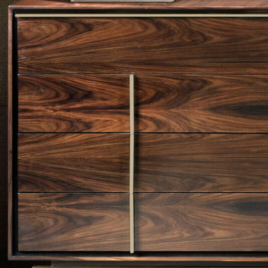 Contemporary Elegant Double Dresser The Contemporary Elegant Double Dresser is crafted from wood and features six drawers with a rich, dark brown wood grain. Two vertical metal handles are centered, accentuating the natural patterns and swirls in the wood. The cabinet corners boast a slightly worn, dark metal frame for an added touch of elegance.