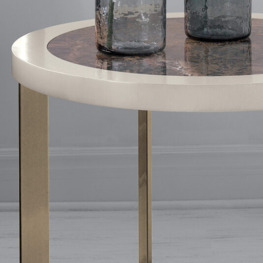 A sleek round Contemporary Marble Top Side Table with a light-colored, smooth cylindrical base. The tabletop features a dark, reflective marble surface and is adorned with two elegant glass containers. The backdrop includes a plain wall and light gray flooring.