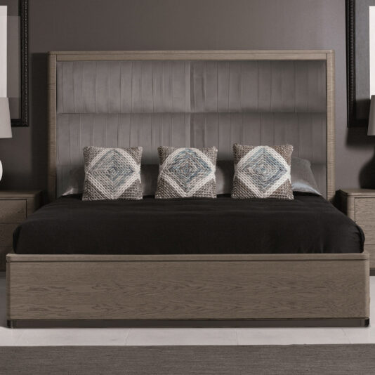 A modern bedroom showcases the Contemporary Oak Veneer Upholstered Bed, which features a tall, stylish upholstered headboard. The bed is dressed in black bedding and adorned with three patterned pillows in the center. Complementary wooden nightstands flank either side of the bed, each topped with a lamp.