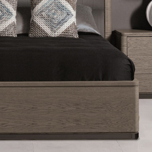 A stylish bedroom featuring a Contemporary Oak Veneer Upholstered Bed with a black bedspread. The bed is adorned with two accent pillows that have gray, white, and blue geometric patterns. A matching wooden nightstand with a round white lamp sits next to the upholstered bed.