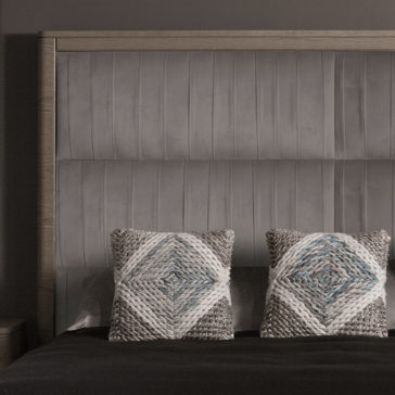 Contemporary Oak Veneer Upholstered Bed A neatly made bed showcases the Contemporary Oak Veneer Upholstered Bed, highlighted by its headboard with vertical stitching. Two decorative pillows featuring a textured diamond pattern in shades of grey and blue are symmetrically placed against the headboard. The dark-colored bedding enhances the minimalistic and cozy ambiance.