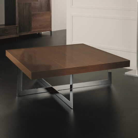 The Contemporary Square Coffee Table features a smooth, rectangular wooden top and a metallic, crisscross leg design. It is set against a minimalistic room with white and wooden paneling and a dark floor.