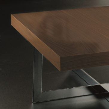 A close-up view of a Contemporary Square Coffee Table with a sleek, polished wooden surface and metal legs on a dark background. The table boasts a minimalist design perfect for any stylish workspace.