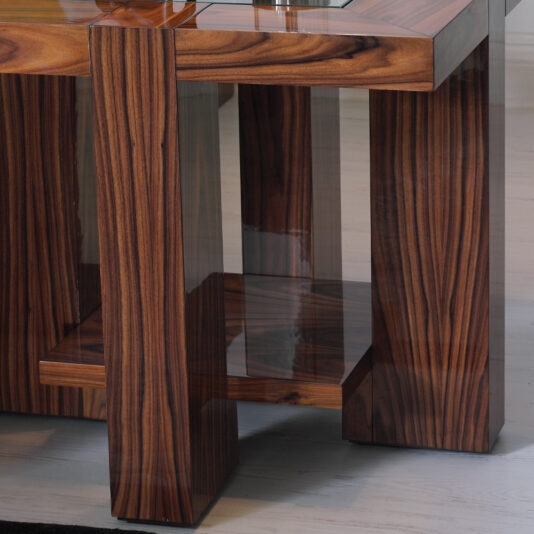Contemporary Square End Table With Glass Top A close-up of the Contemporary Square End Table With Glass Top reveals its polished wooden surface with rich, dark grain patterns. The table features a robust rectangular design, complemented by thick legs and an additional shelf underneath. The glossy finish of the wood reflects light beautifully, while intricate natural textures adorn the surface.