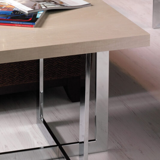 A sleek, modern coffee table with a light wooden top and metallic legs serves as the centerpiece. On the Contemporary Wooden End Table, an open magazine displays vibrant images alongside an angled smartphone. The flooring beneath is light-colored with a subtle texture.