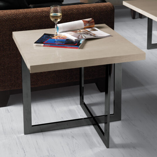 A **Contemporary Wooden End Table With Black Base** is placed near a brown upholstered chair. The table holds an open magazine, a wine glass filled with white wine, and a few magazines stacked on it, all set against a light wooden floor.
