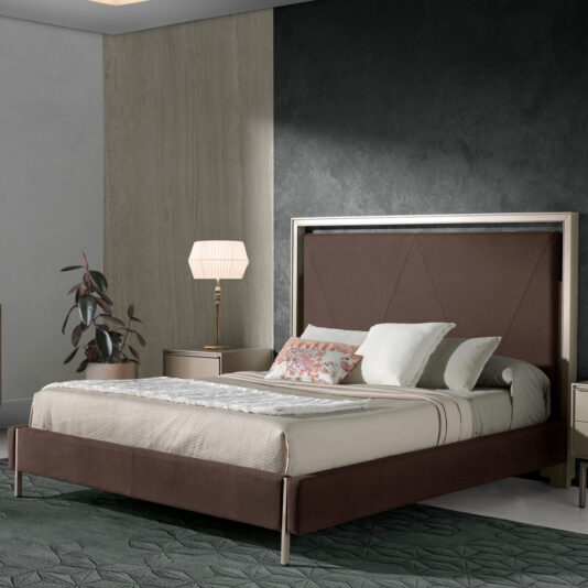 A modern bedroom showcasing the Deluxe Modern Upholstered King Size Bed, which features a dark brown headboard and frame. The bed is adorned with white and patterned pillows, along with a beige duvet. On either side of the bed, nightstands with lamps provide balance to the space. A potted plant is strategically placed near one of the nightstands for an added touch of nature.