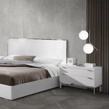 Modern bedroom with a Deluxe Miami Style White Lacquered Bed, featuring a high-gloss headboard and neutral bedding. Beside the bed, a white nightstand holds a small speaker, stacked books, and geometric light fixtures with spherical bulbs hanging above. The room has a minimalist design.