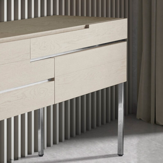 An Elegant Sideboard With Drawers, showcasing minimalist design with light wooden construction and clean lines, stands against a backdrop of vertical slatted wooden panels. The sophisticated desk features multiple compartments with sleek, integrated handles and metallic legs, all positioned on a floor of light-colored tile.