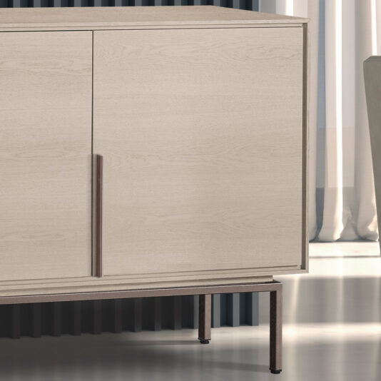 A close-up view of the Elegant Sideboard With Metal Base reveals its modern, light wood finish and two doors that feature sleek metal handles and thin, angled metal legs. Positioned indoors against a backdrop of vertical black slats and white curtains, the sideboard exudes sophistication.