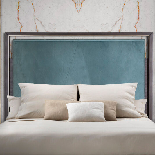 The Elegant Metal Frame Bed boasts a stylish blend of modernity and elegance with its sleek metal construction and padded blue headboard. Positioned against a white marble-patterned wall, the bed is beautifully adorned with five cushions in various shades of beige, white, and brown, each meticulously arranged for a tidy appearance. The overall ambiance exudes both coziness and contemporary charm.