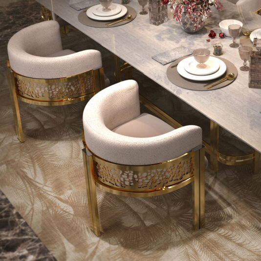 A luxurious dining setup featuring a sleek table with a beige marble top, adorned with elegant tableware, wine glasses, and floral decorations. The Exclusive Curved Dining Chairs, upholstered in gold and beige with ornate gold bases, surround the table and are placed on a patterned carpet.