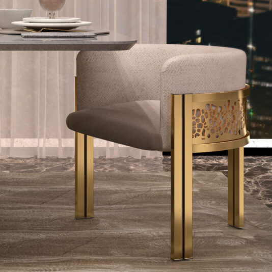 An Exclusive Curved Dining Chair with an elegant design, featuring gold metal legs and a decorative gold backrest panel, is upholstered in light beige fabric. It is positioned next to a glass-topped dining table, with a cityscape visible through a nearby window.