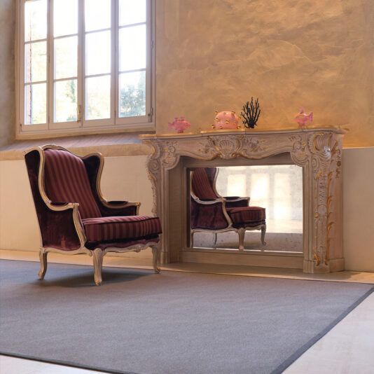 High Backed Venetian Style Armchair A luxurious room featuring a large window with multiple panes, an ornate mirror above a decorated mantel, and an elegant High Backed Venetian Style Armchair with red and black striped upholstery. The walls have a textured finish in light and warm colors, and the floor is covered with a gray rug.