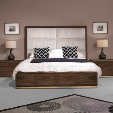 High End Contemporary Chest Of Drawers A modern bedroom featuring a large bed with a wooden frame and a padded headboard, adorned with two patterned cushions and a white pillow. The room includes matching wooden nightstands with lamps, the High End Contemporary Chest Of Drawers, framed pictures on the wall, and a decorative rug on the floor.