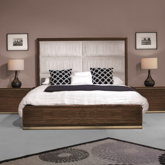 A modern bedroom featuring a large bed with a wooden frame and a padded headboard, adorned with two patterned cushions and a white pillow. The room includes matching wooden nightstands with lamps, the High End Contemporary Chest Of Drawers, framed pictures on the wall, and a decorative rug on the floor.