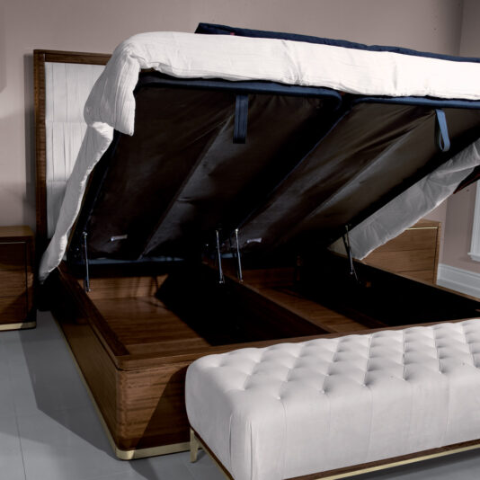 A modern wooden bed frame with a raised mattress showcasing built-in under-bed storage is positioned against a wall. A white tufted bench sits at the foot of the bed. The open, spacious compartments perfectly complement the High End Contemporary Chest Of Drawers in the room.