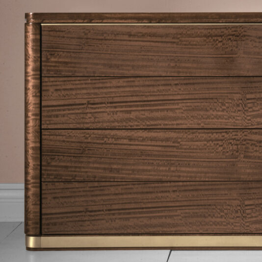 High End Contemporary Chest Of Drawers A close-up of the High End Contemporary Chest Of Drawers showcases its distinctive grain patterns and horizontal lines, underscoring its elegant design. The chest boasts a polished finish with metallic accents along the edges, elegantly positioned against a light wall and tiled floor.