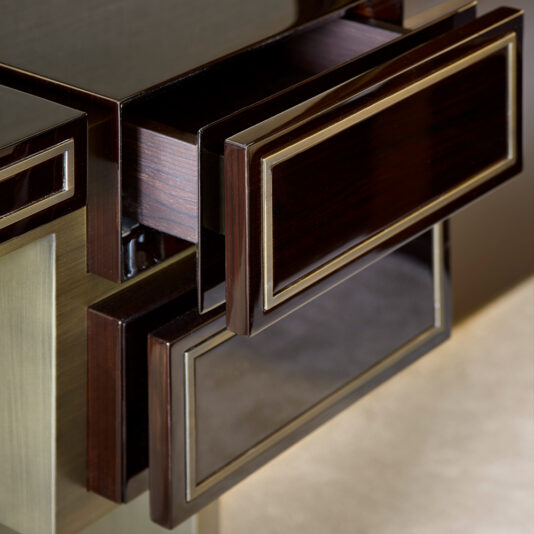 High End Contemporary Dressing Table Close-up of the High End Contemporary Dressing Table showcasing its sophisticated design with two drawers featuring sleek, geometric lines and metallic accents. The drawers boast a dark wood finish with elegant gold trimming, highlighting a modern and polished aesthetic. One drawer is partially open, revealing the interior.