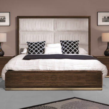 Contemporary Pleat Upholstered Bed A contemporary bedroom featuring the Contemporary Pleat Upholstered Bed, characterized by its large pleated design and dark wood frame. The bed is dressed in white bedding with black and white patterned accent pillows. Two matching bedside tables, each with a lamp, flank the bed, while framed artwork adorns the wall.
