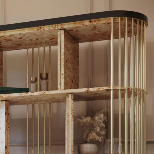 Large Modern Art Deco Style Bookcase A close-up of the Large Modern Art Deco Style Bookcase, showcasing its wooden shelves with a speckled pattern and gold-finished vertical metal rods that support the structure. The bookcase displays a green book, two small glass vases, and a pot with dried pampas grass.