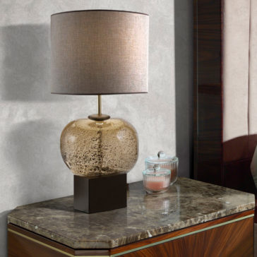 Luxury Dark Rosewood Bedside Table A modern table lamp with a textured glass base and a beige drum shade is elegantly placed on the Luxury Dark Rosewood Bedside Table, which features a polished marble top. Beside the lamp, a glass jar and a small pink candle sit neatly on the table's surface.