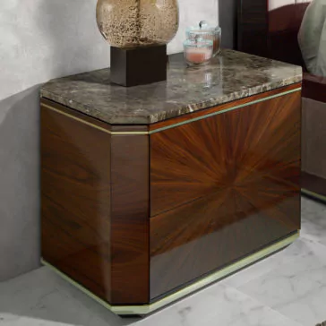 Luxury Dark Rosewood Bedside Table Against a light wall stands the sleek and modern Luxury Dark Rosewood Bedside Table, featuring a glossy wood finish and a marbled top. This elegant nightstand comes with two drawers for convenient storage. On top, a decorative lamp with a textured surface accompanies a glass container filled with small trinkets.