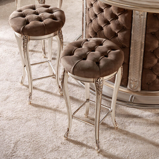Luxury Italian Bar Stool Two **Luxury Italian Bar Stools** with tufted brown velvet seats and ornate light-colored legs placed on a plush beige carpet evoke the charm of opulent dressing table stools. The bar behind them features a matching tufted design, creating a cohesive and sumptuous setting.