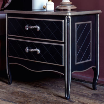 Luxury Italian Horse Handle Bedside Cabinet The Luxury Italian Horse Handle Bedside Cabinet showcases a luxurious black finish with two drawers adorned by diamond-patterned fronts and silver horse-shaped handles. This elegant nightstand features curved legs and a polished wooden top, complemented by its placement on a hardwood floor. A lamp with a white base and beige shade adds the finishing touch to this sophisticated setting.
